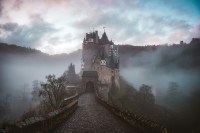 a photo of a gothic castle in the mountains surrounded by fog
